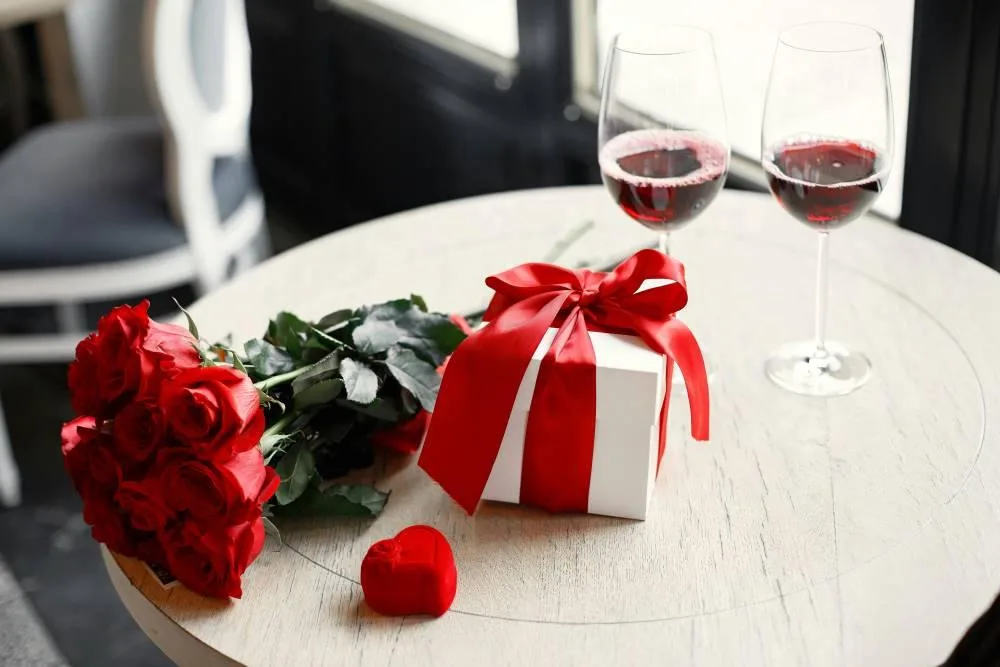 Red roses, gift box and wine on a romantic table
