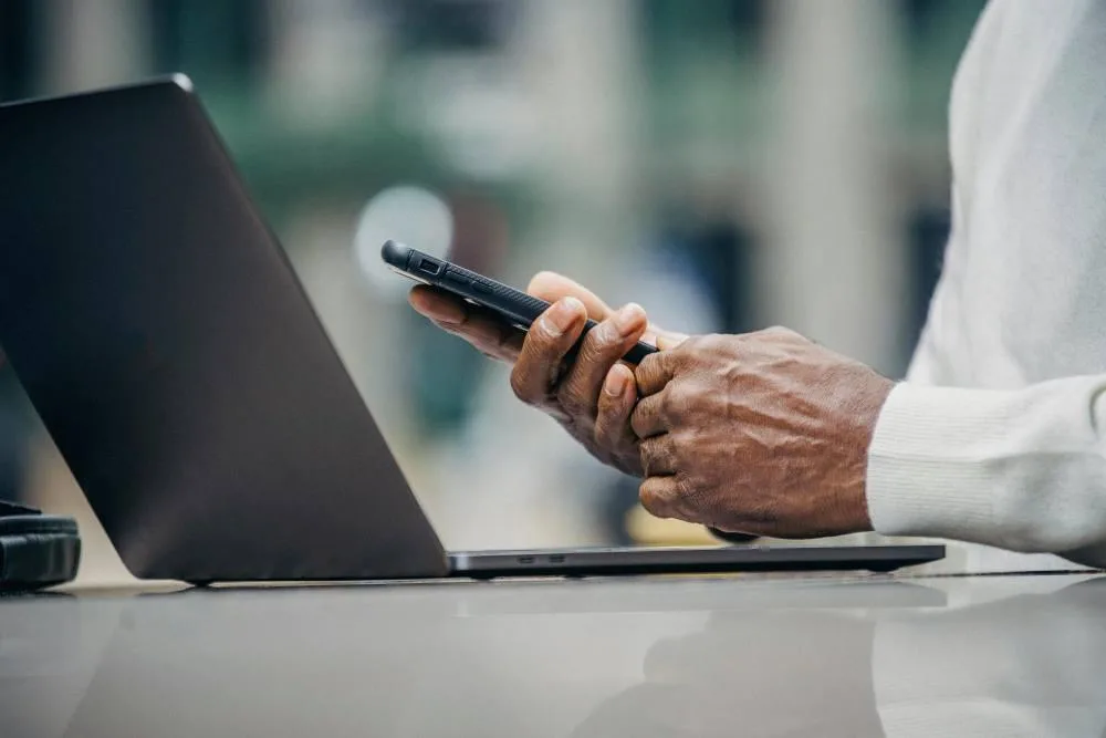 A gentleman holding a phone whilst on a laptop
