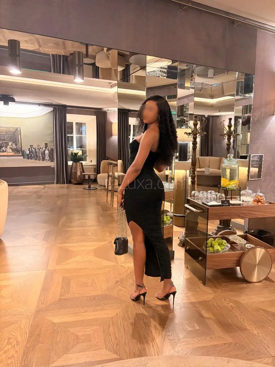 Woman in black ruched dress posing in elegant hotel lobby.