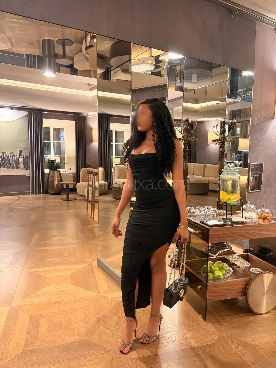 Woman in a black ruched dress posing in a lounge.