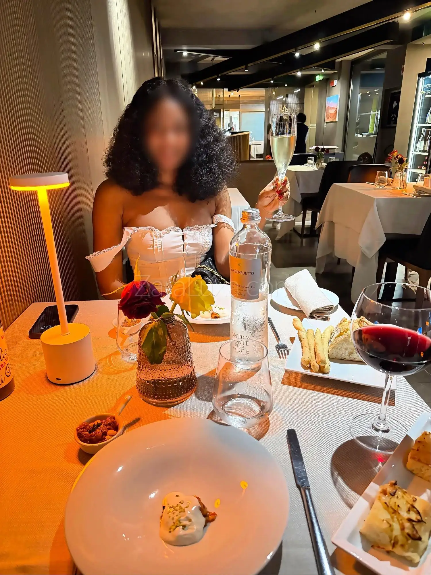 Woman toasts with champagne at an elegant restaurant dinner table.