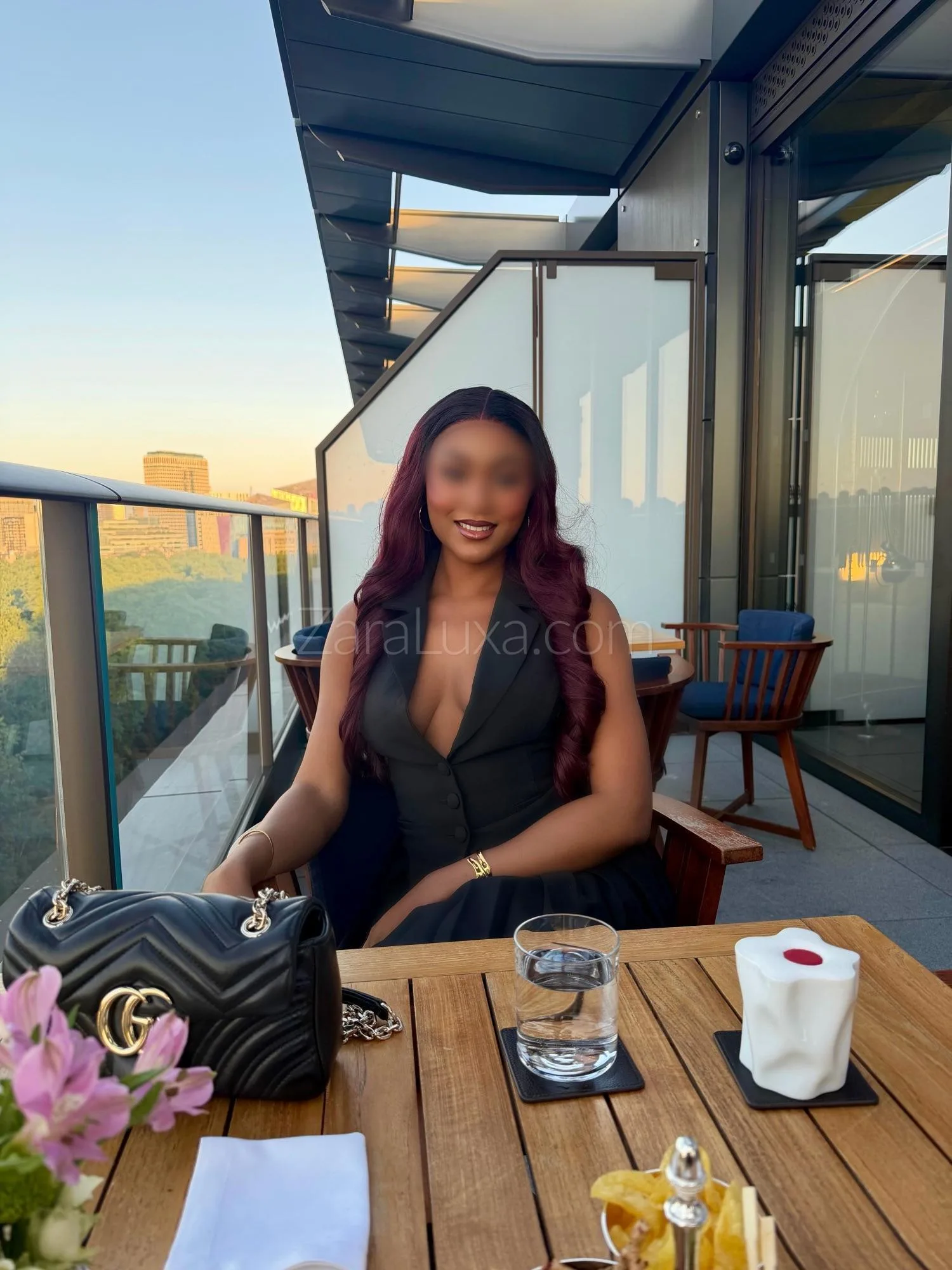 Woman in a black dress at a rooftop restaurant table.