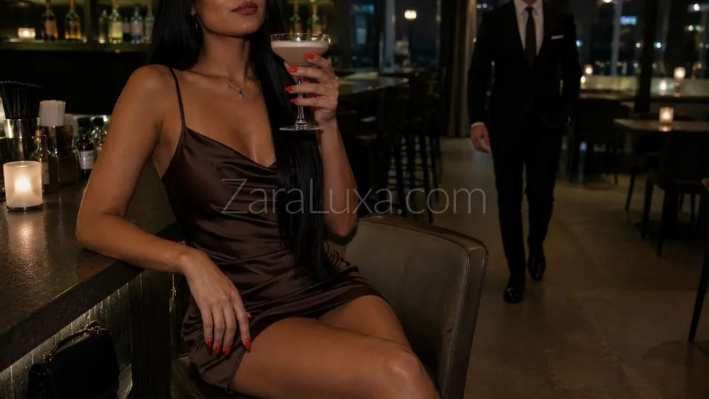 Woman in brown silk slip dress holding cocktail at bar